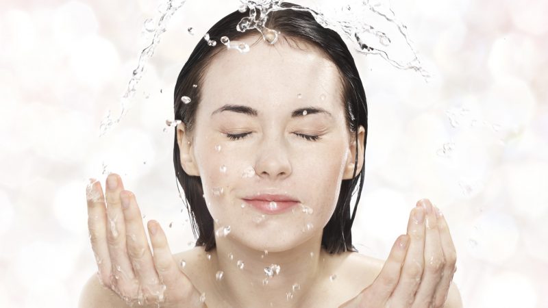 Young woman washing her face with cold water