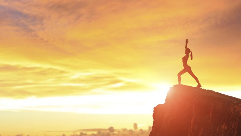 Young woman silhouette practicing yoga on top of mountain with sunshine at sunset