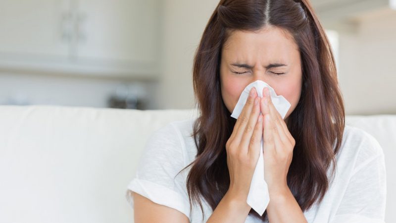 Brunette sneezing in a tissue in the living room; Shutterstock ID 114498919; PO: today.com